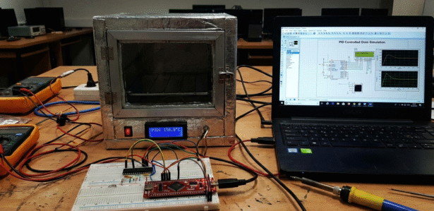 PID-controlled oven prototype with microcontroller and laptop simulation on a lab bench.